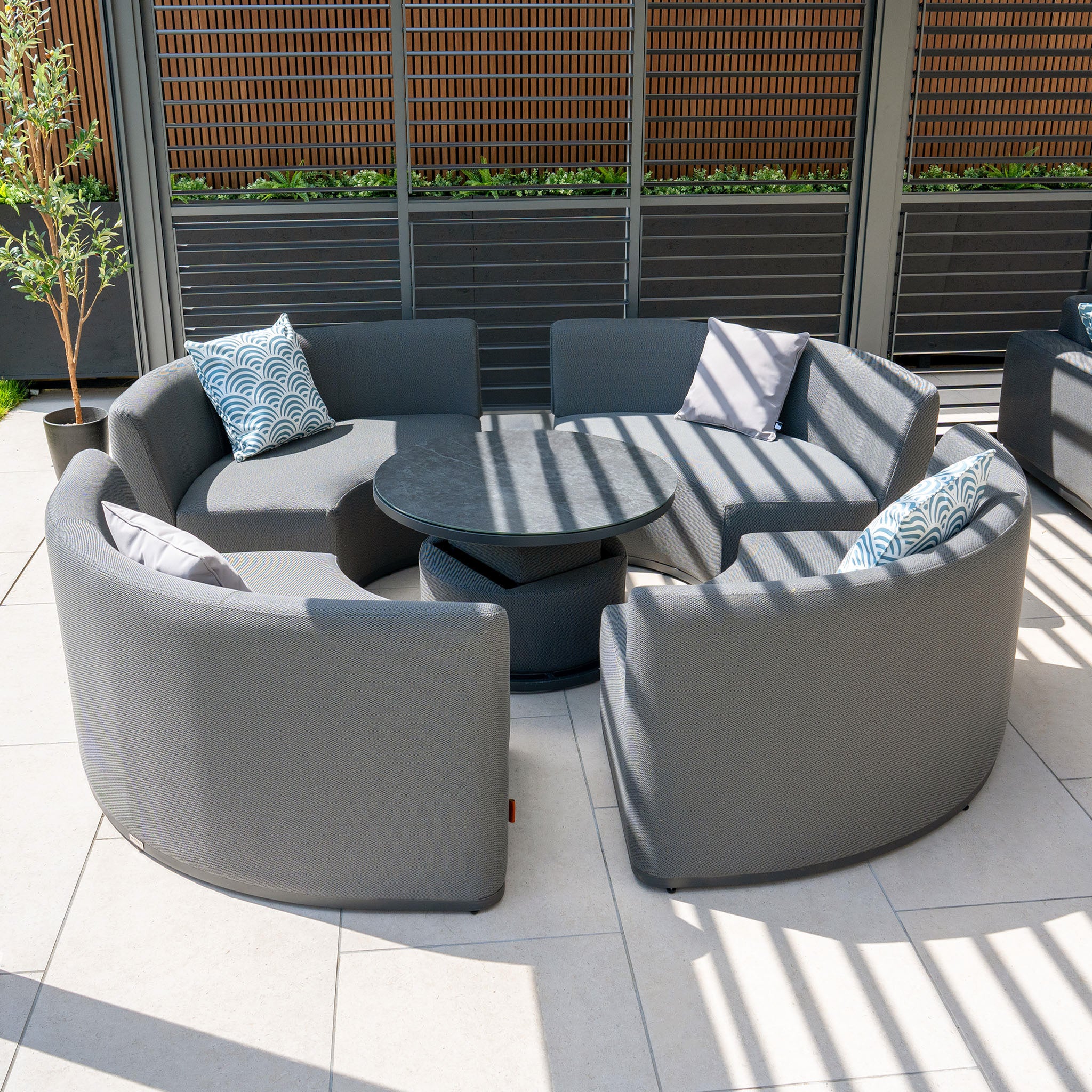 Circular outdoor seating arrangement featuring the Luna Outdoor Fabric Lifestyle Suite with 4 Sofas in Grey and a round coffee table on a tiled patio.