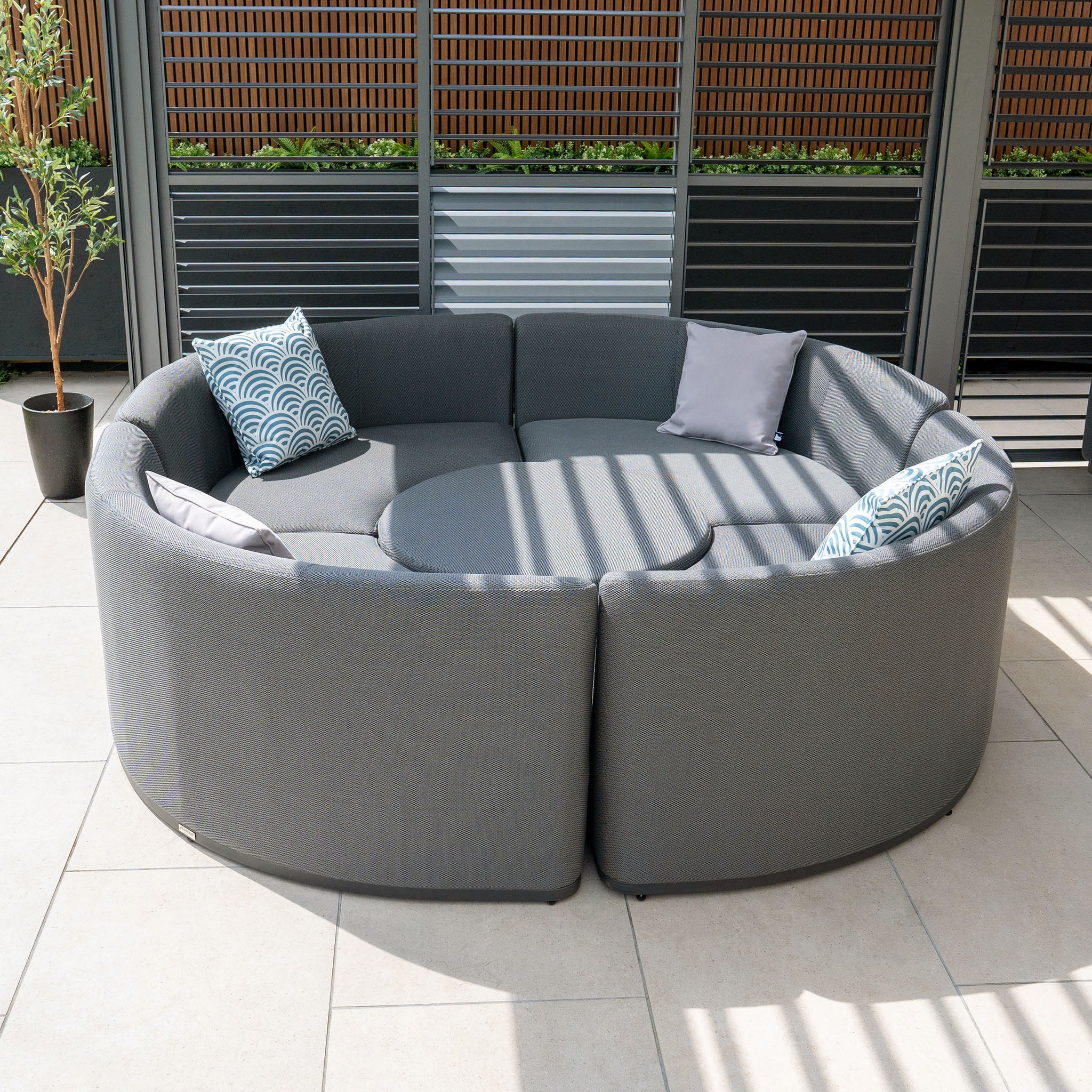 Luna Outdoor Fabric Lifestyle Suite with 4 Sofas in Grey, featuring cushioned seats and pillows made from all-weather material, arranged in a circular pattern on a patio with tile flooring.