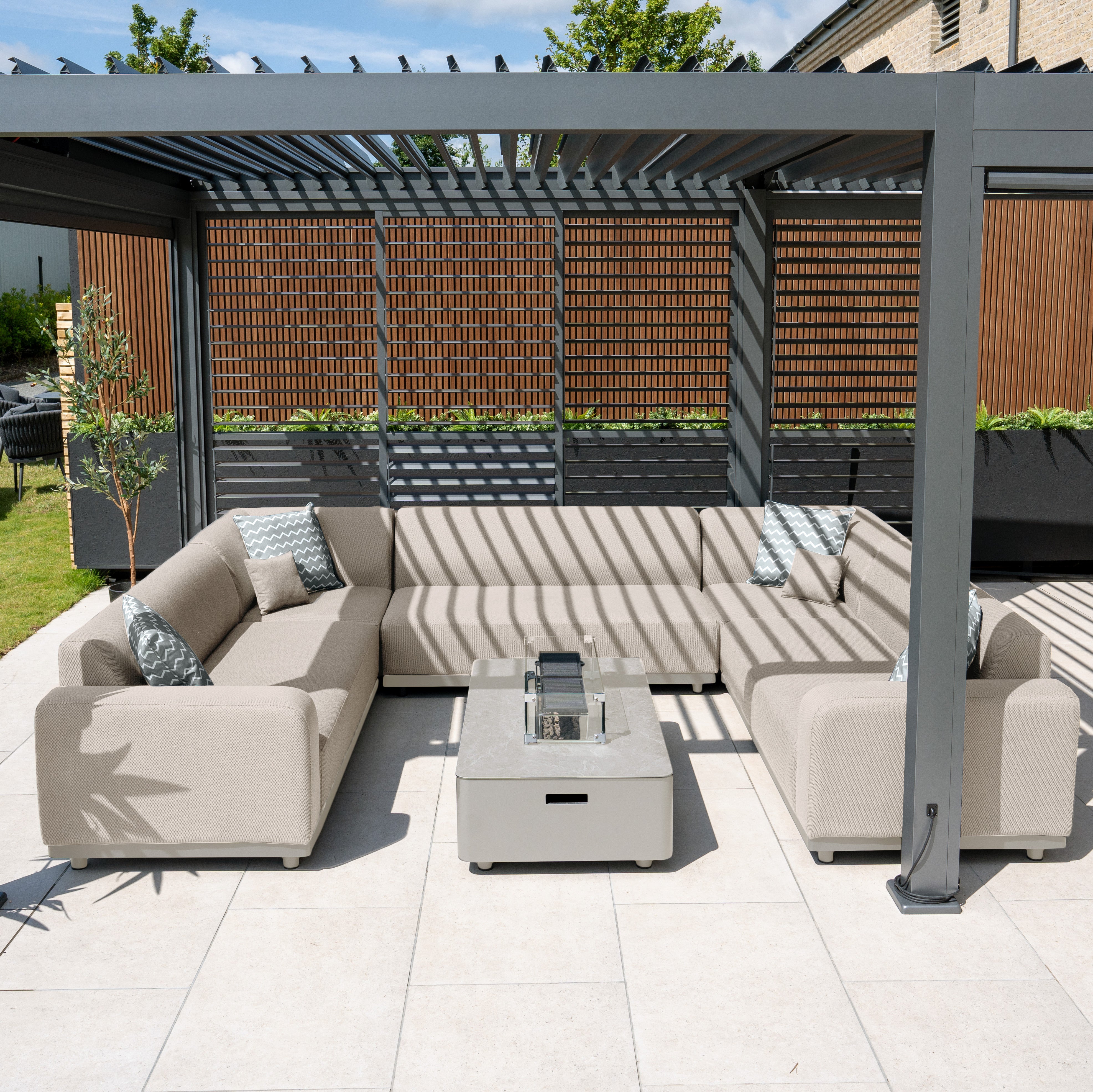 The outdoor space boasts the Luna U-Shape Outdoor Fabric Sofa Set with Firepit Coffee Table in Fawn, complemented by a stylish pergola on tiled flooring. This setup is perfect for cozy gatherings, blending functionality with comfort using quick-dry foam and durable outdoor fabric.