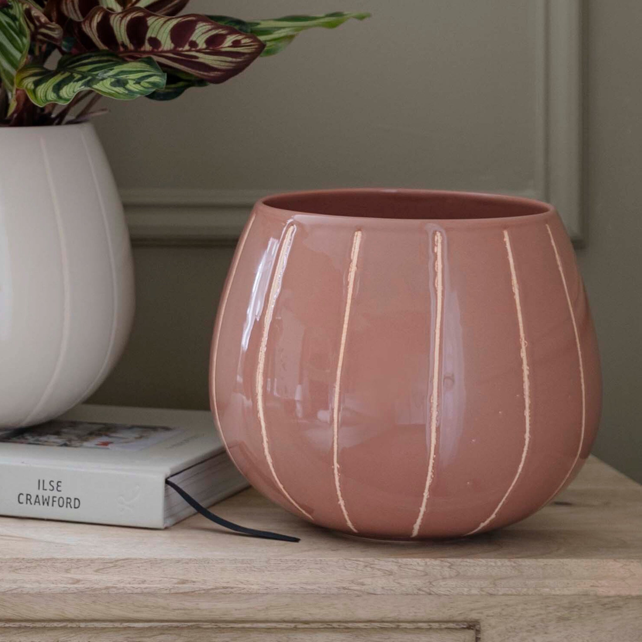 Nova Wax Relief Rose planter on a wooden surface, next to a white vase with a plant, and a book titled "Ilse Crawford".