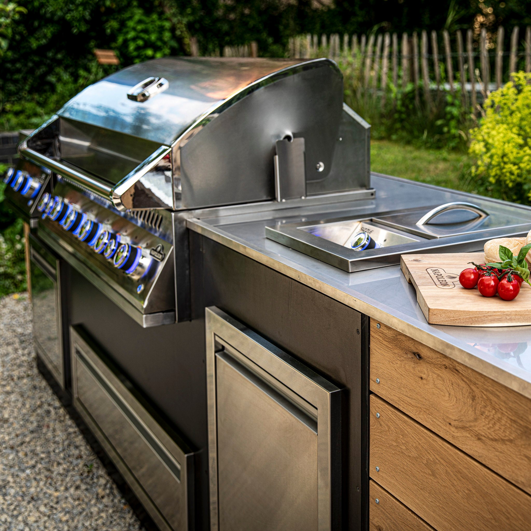 Outdoor kitchen featuring a Napoleon 700 Series 44" Built-in Gas Grill, wooden countertop, vegetables on a cutting board, and a sink.