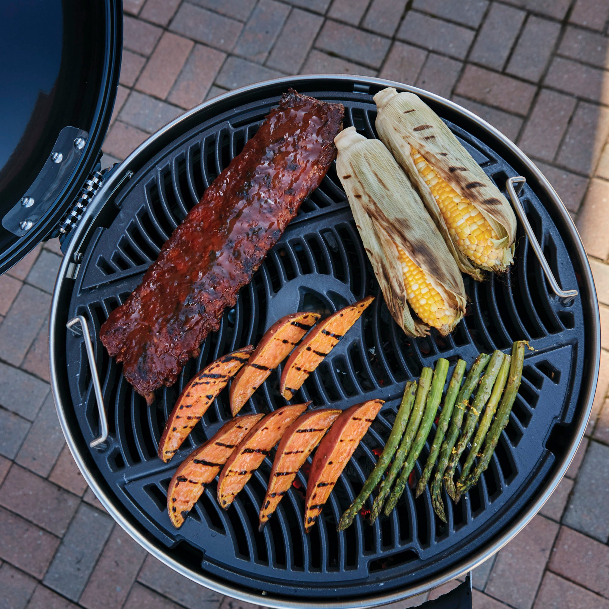 Grill ribs, corn on the cob, sweet potato wedges, and asparagus on a brick patio using the Napoleon Pro Charcoal Kettle Grill for precise temperature control.