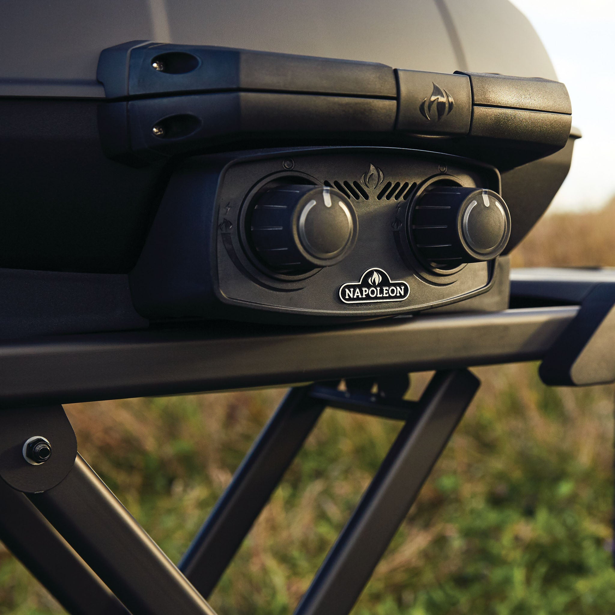 Close-up of a Napoleon Phantom TravelQ Pro 285X Portable Gas Barbecue showcasing its control knobs and the brand logo, with grass in the background, perfect for gourmet portable grilling.