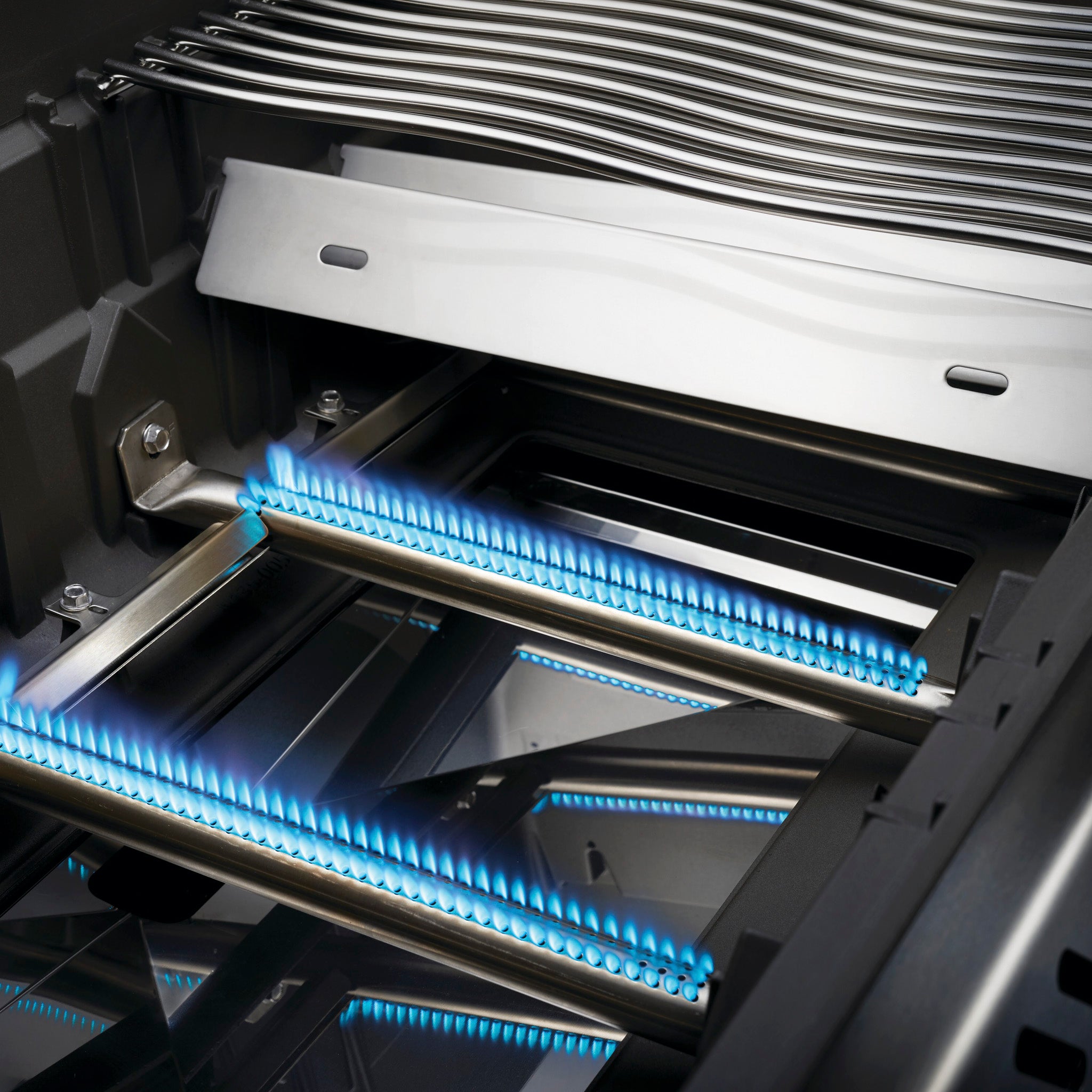 Close-up of a lit Napoleon Rogue 525 Gas Barbecue with blue flames emanating from two burners beneath the stainless steel grates, beautifully illustrating its precise temperature control.