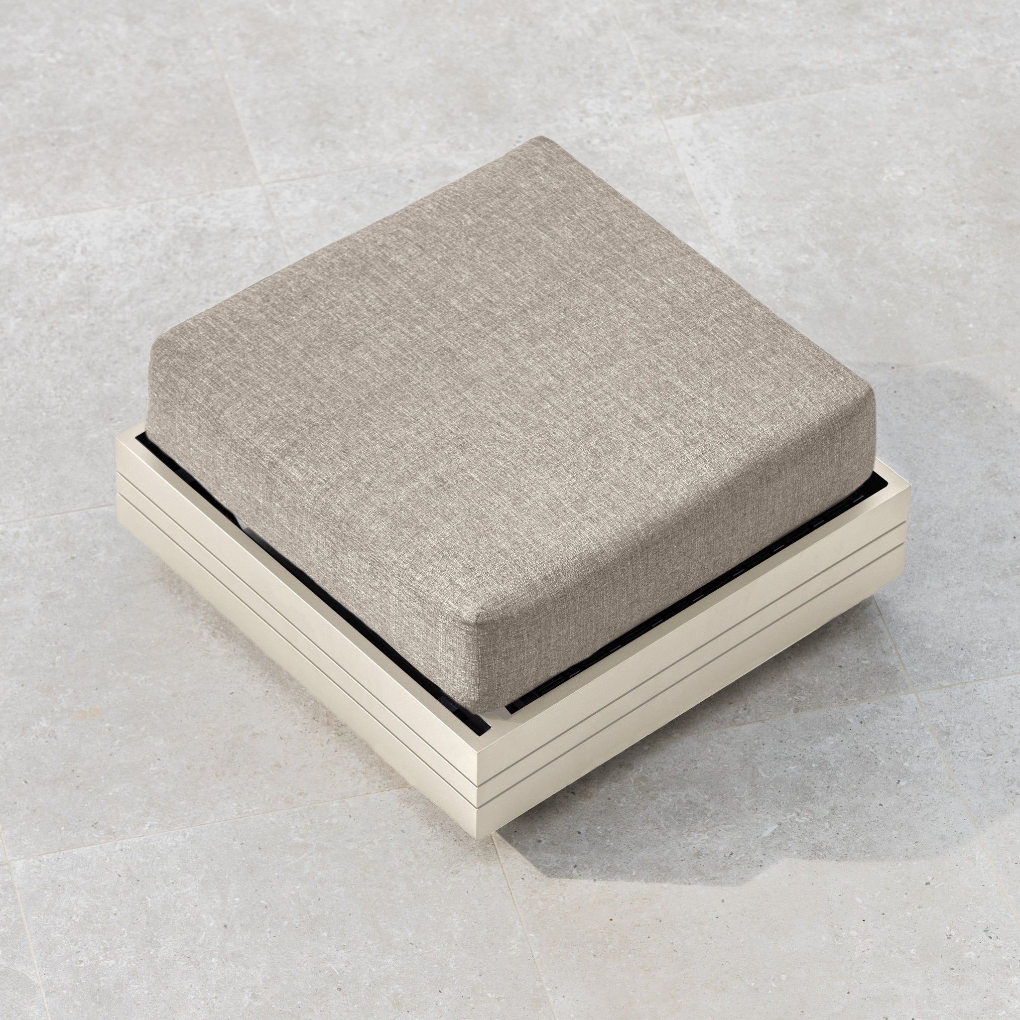 The Panama Corner Unit/Footstool in Latte, featuring a beige cushion on a square, light-colored wooden base, is placed elegantly on a light stone floor.