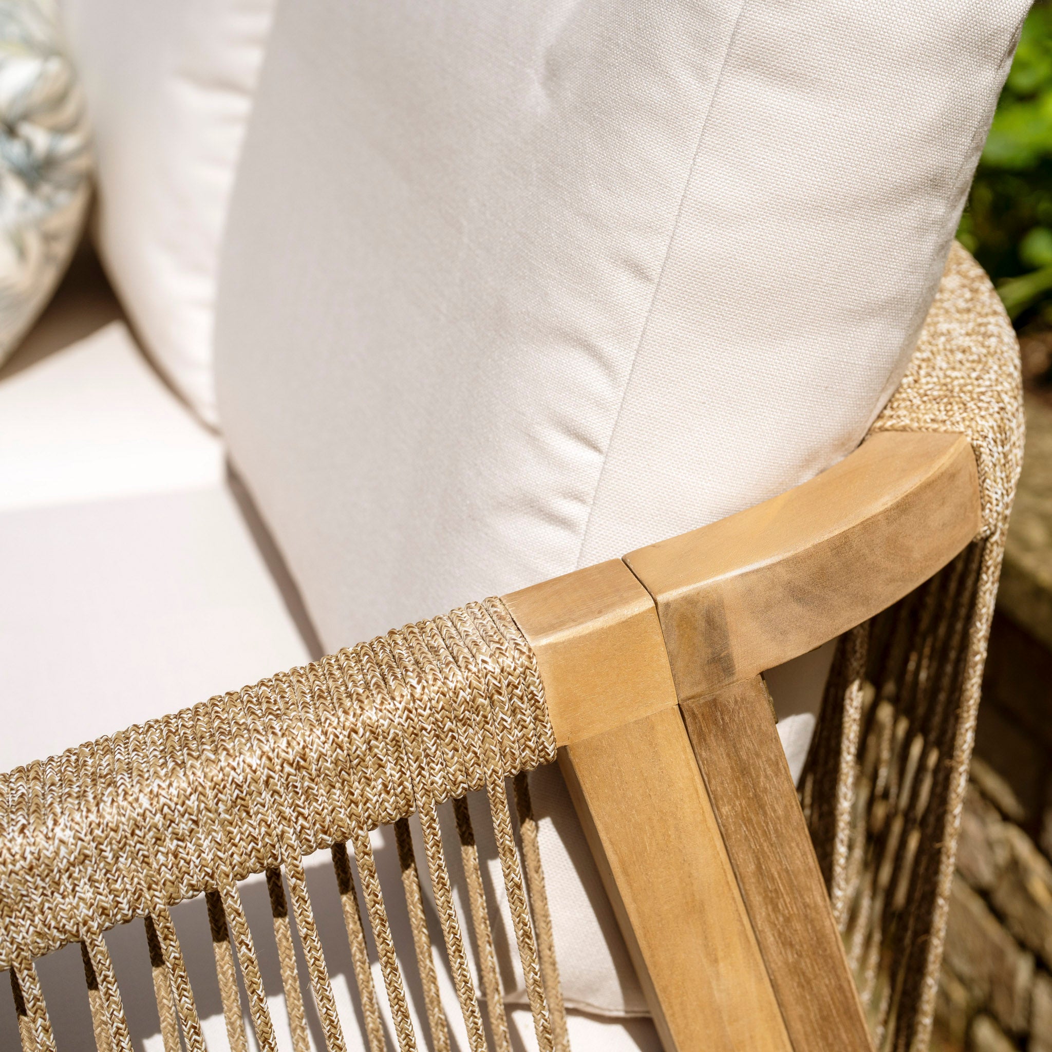 Close-up of the Quay Corner Dining Set with Armchair in Linen, featuring a beige cushioned outdoor chair with wooden and woven rope armrest details, crafted from sustainably sourced acacia wood.