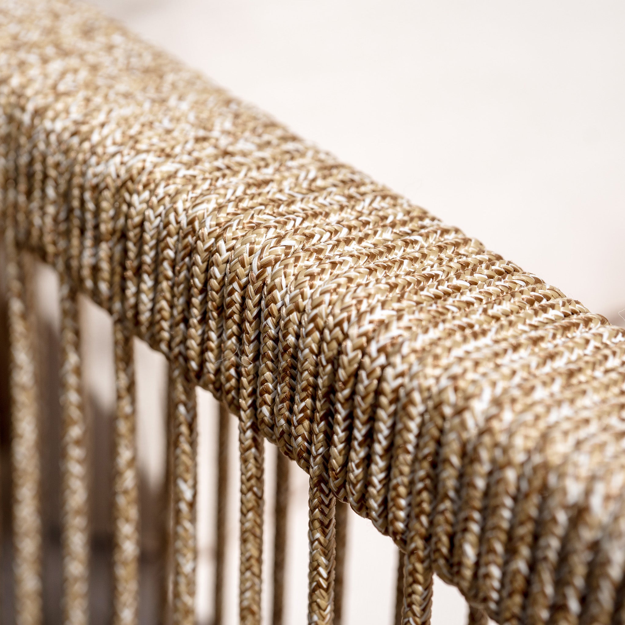 Close-up of beige and white woven rope detail on the back of a chair, with hanging strands below. This elegant piece is part of the Quay Corner Dining Set with Armchair in Linen, featuring sustainably sourced acacia wood and designed to enhance your outdoor furniture collection.