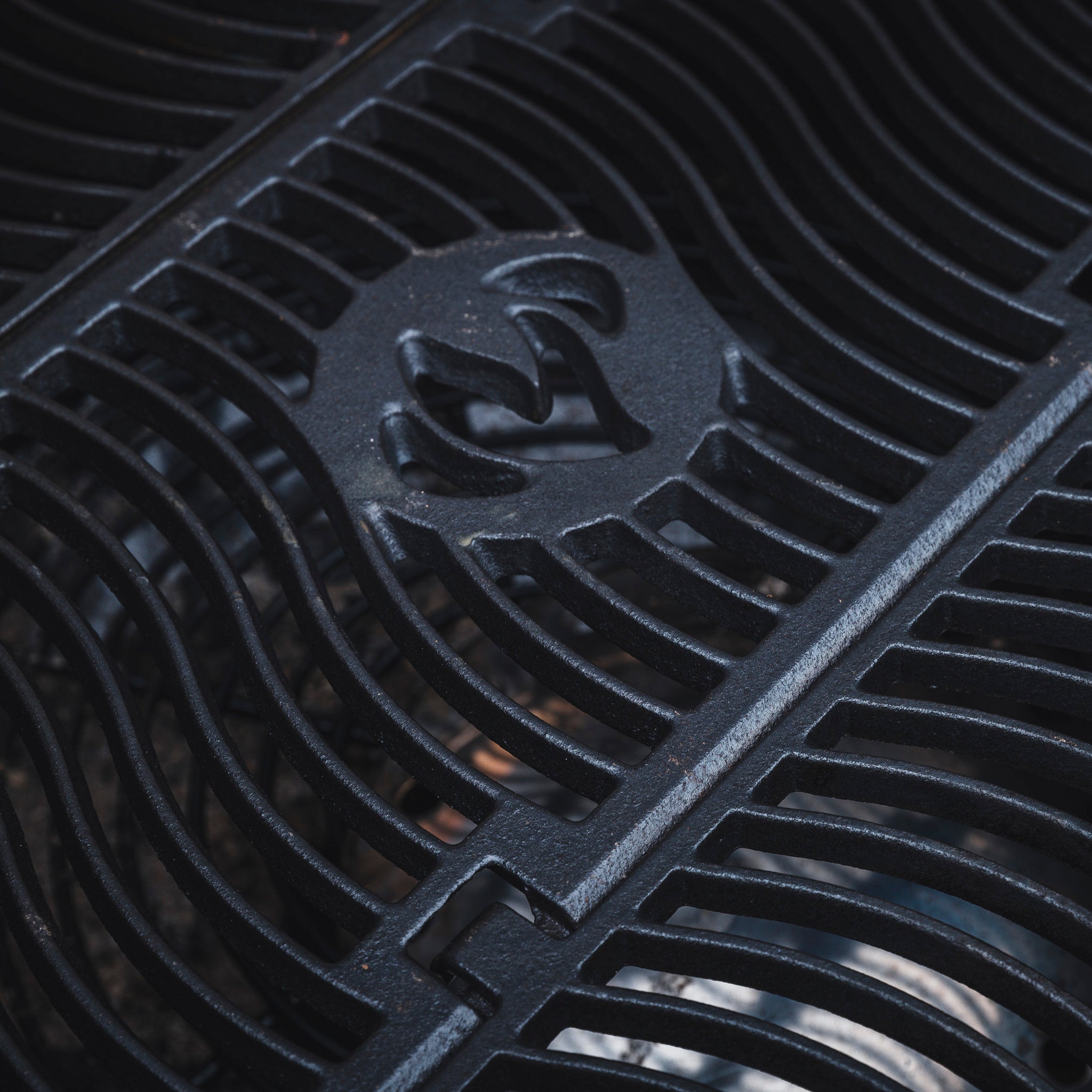 Close-up of black metal grating with geometric patterns and a curved emblem in the center, showcasing the sleek design of the Napoleon Rogue 425 Gas Barbecue. This grill ensures precise temperature control for optimal cooking results.