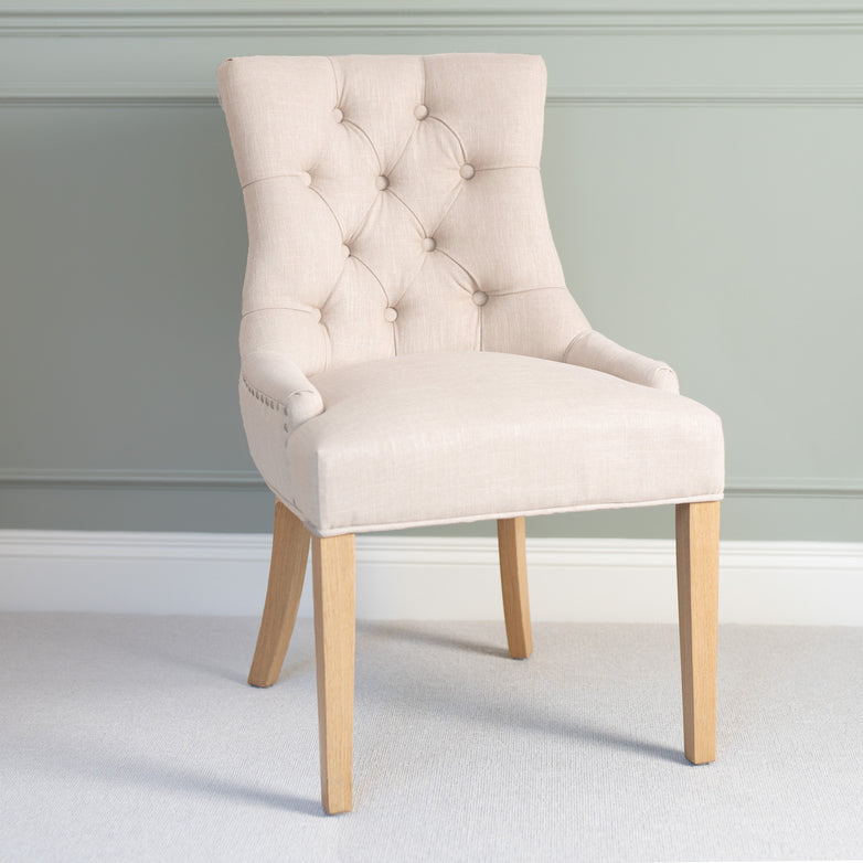 The Regent Chair Set of 2 in Ivory, featuring a sleek tufted backrest and wooden legs, complements a soft green paneled wall with its contemporary design inspired by classic Regent Chairs.