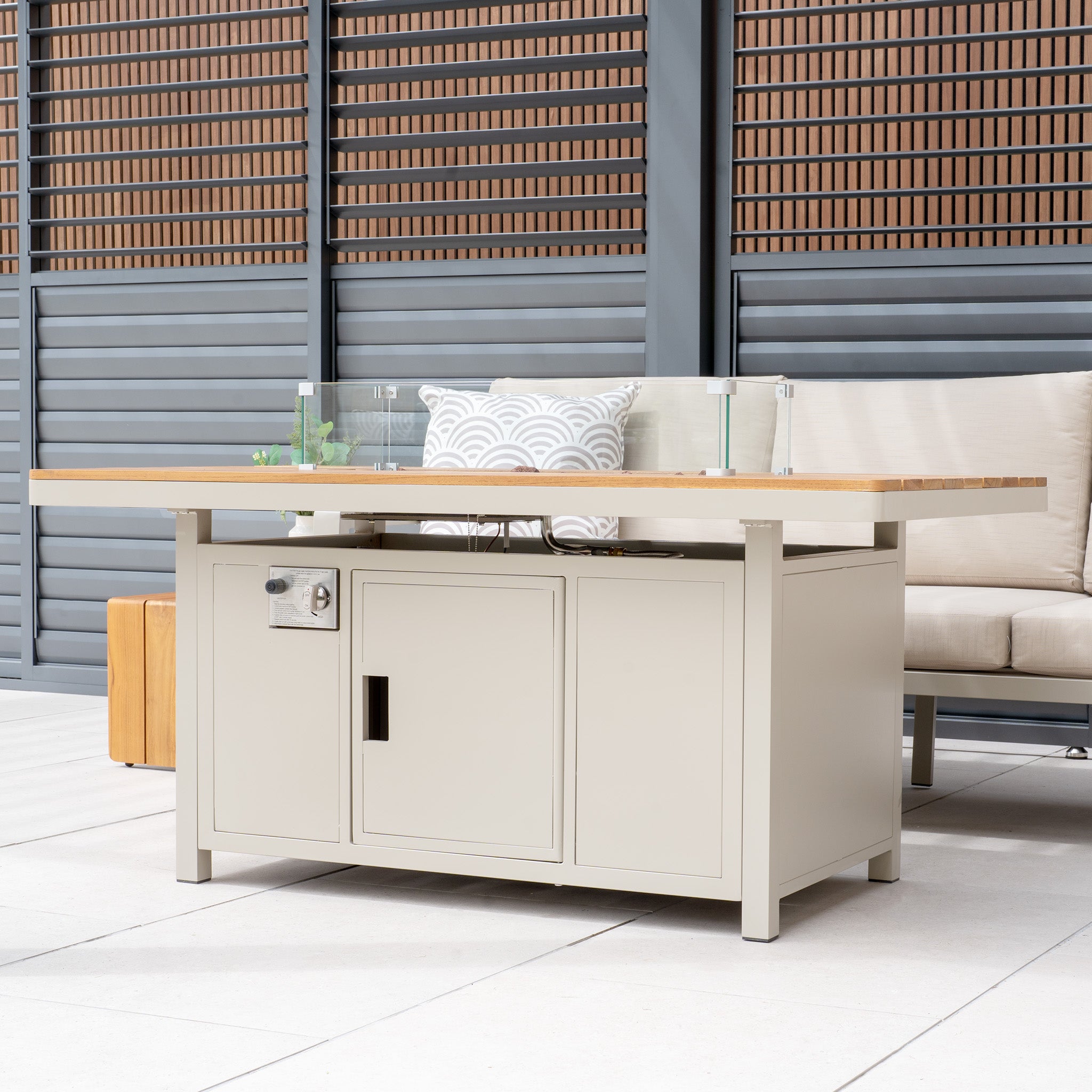 Stockholm Corner Dining Set with Firepit Table in Limestone, arranged on a patio with beige cushioned garden furniture and decorative pillows.