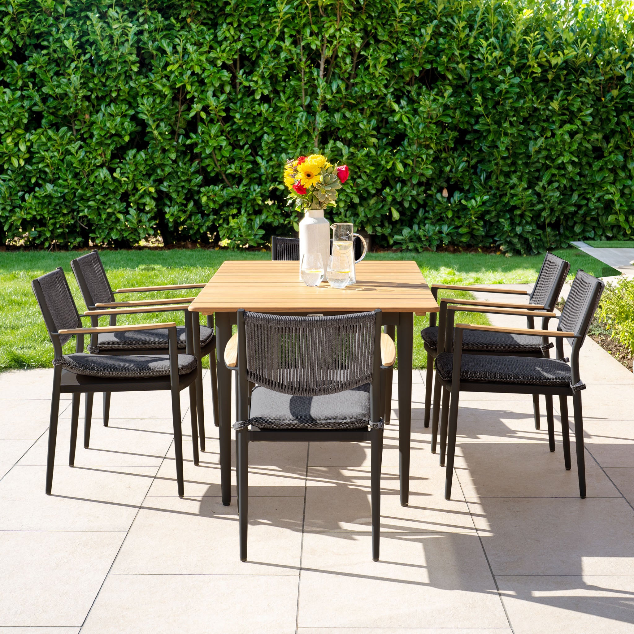 The Tellaro 6 Seat Rectangular Dining Set with a teak table in charcoal includes six black chairs, adding elegance to any patio setting.