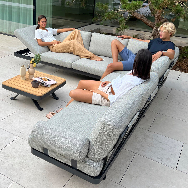 Three people relax on an L-shaped Vienna Corner Group Set in Grey next to a small wooden table on a patio, enjoying premium outdoor living.