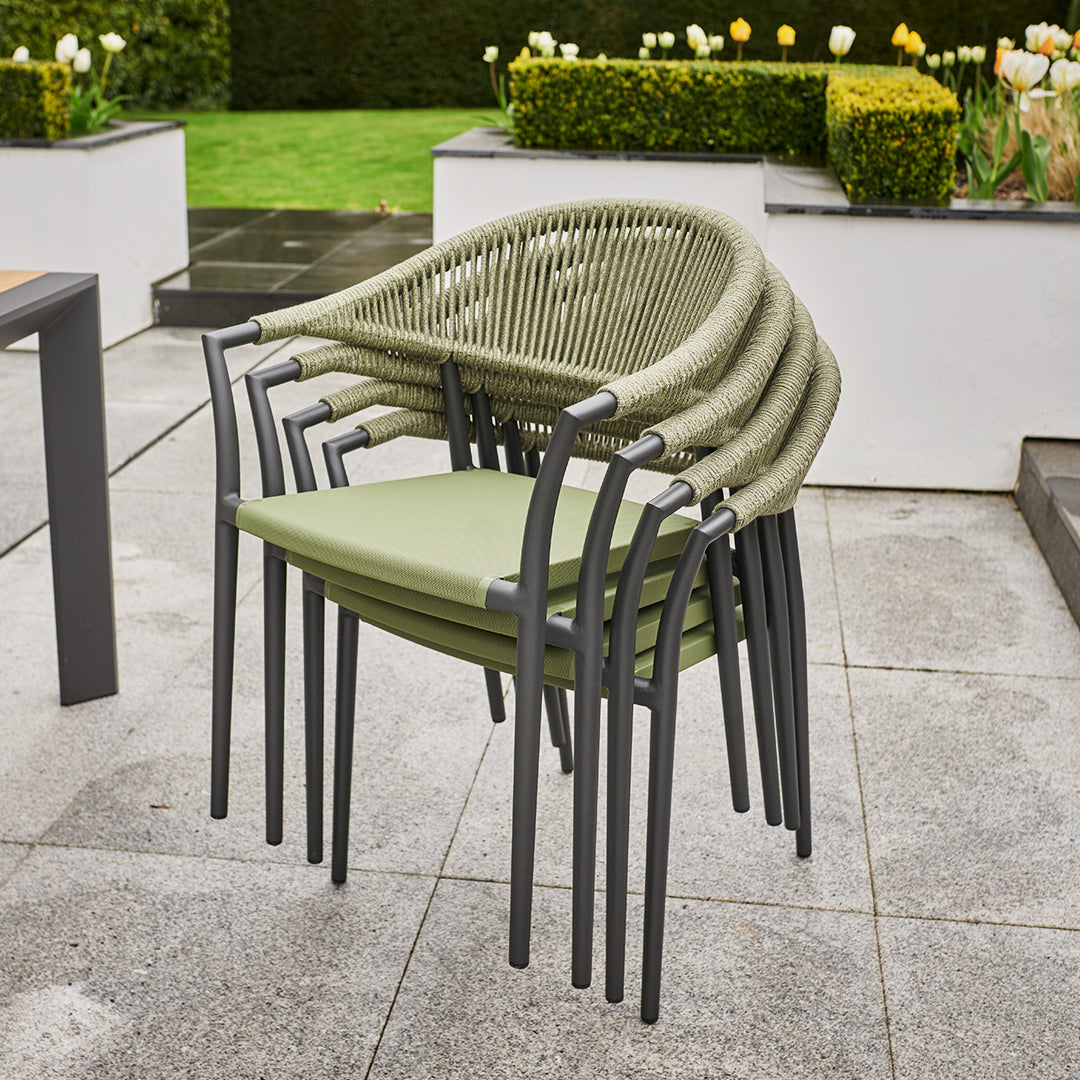 Stacked green patio chairs with grey frames on a tiled outdoor patio feature alongside the Cloverly 8 Seat Rectangular Extending Dining Set with Teak Table in Olive Green, accompanied by white planters and flowers in the background. The weather-proof furniture ensures durability and style for any outdoor space.