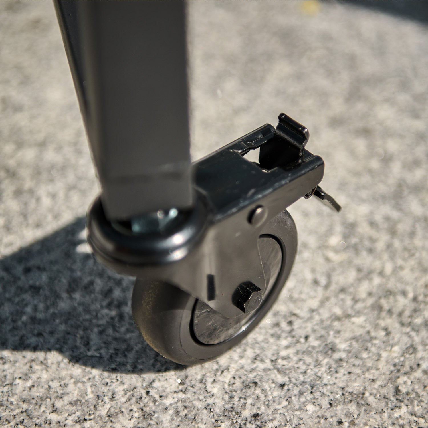 Close-up of a black caster wheel attached to the bottom of a piece of furniture on a textured surface, reminiscent of the sturdy build found on the Kamado BBQ 18" Ceramic Grill in Matte Green.