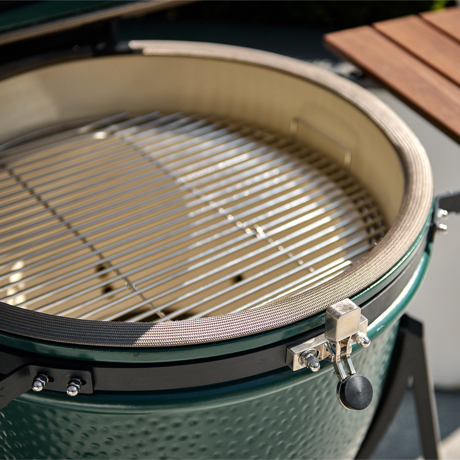 Close-up of an open Kamado BBQ 18" Ceramic Grill in Matte Green with ceramic walls and a stainless steel grate, in bright sunlight.