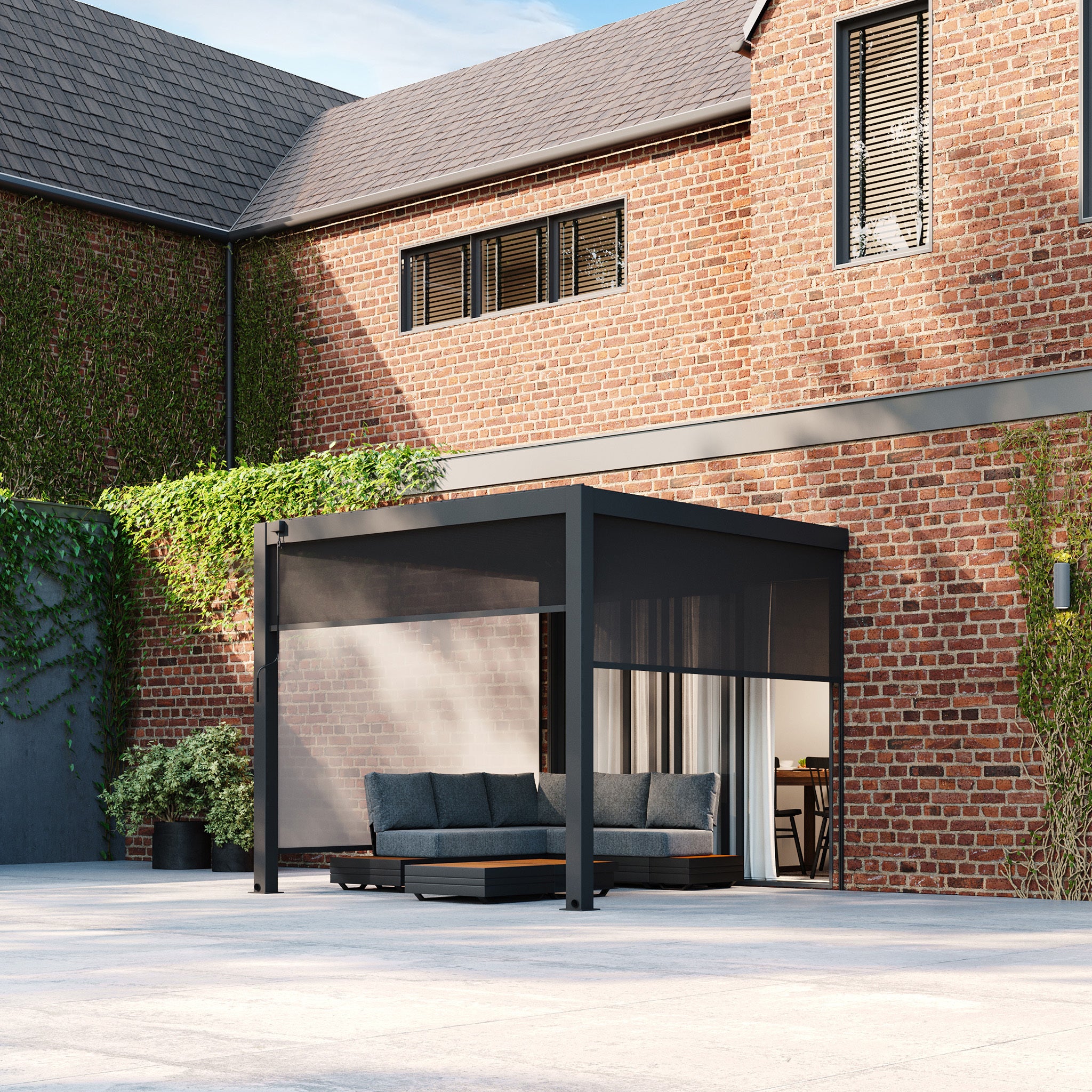 Modern patio with a gray PergoSTET 3m x 3m Square Wall Mounted Pergola featuring 3 drop sides and LED lighting, outdoor seating, and a brick house with ivy and large windows in the background. The built-in drainage system adds practicality without sacrificing style.