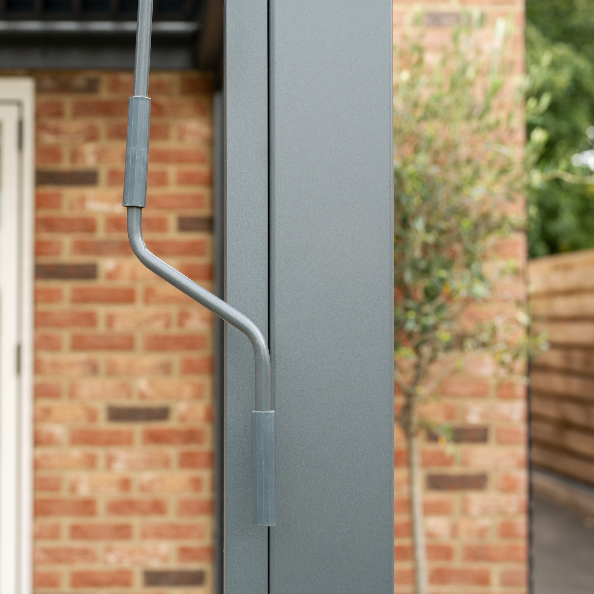 Close-up of the PergoSTET 3m x 3m Square Wall Mounted Pergola's gray metal handle attached to a vertical structure, with a brick wall in the background, exemplifying the sleek modern design.