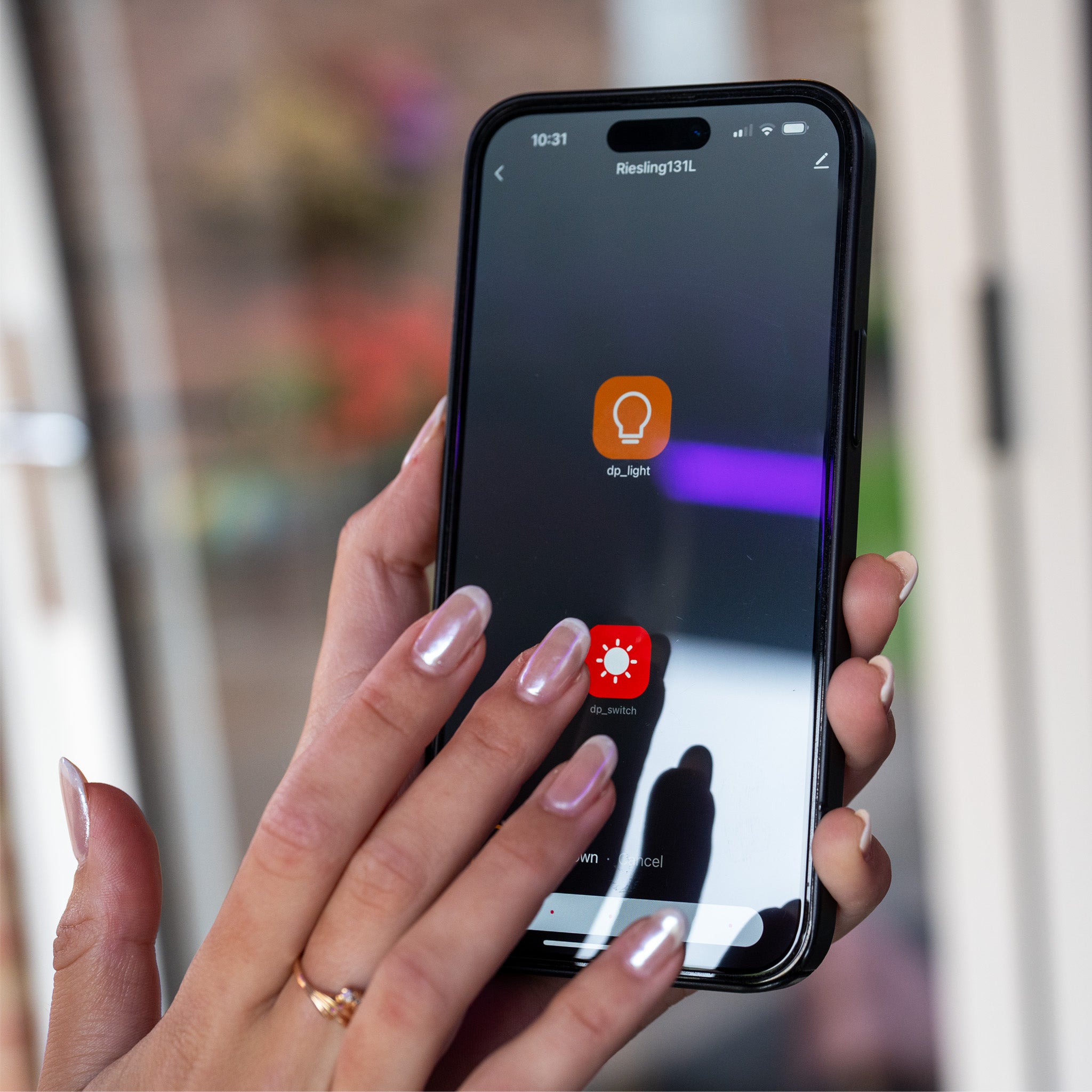 Close-up of a person using a smartphone app to control two smart light bulbs, one orange and one red, under the sleek shadows of the PergoSTET 3m x 3m Square Wall Mounted Pergola with 3 Drop Sides and LED Lighting in Grey.