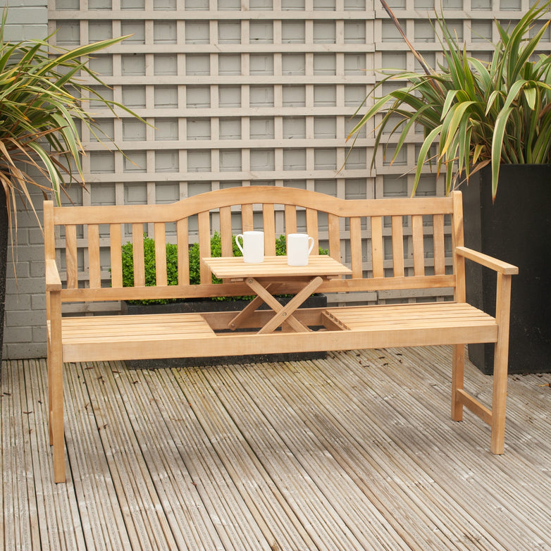 Richmond Antique Wood Bench with Pop Up Table in Light Teak on a patio, holding two white mugs and flanked by potted plants.