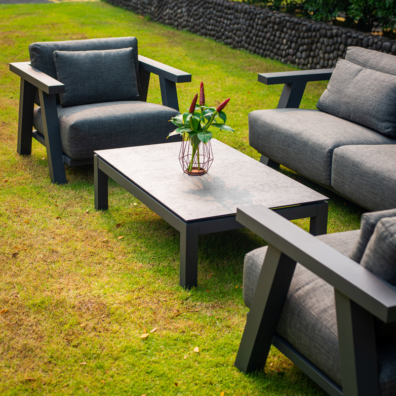 Outdoor seating area with the Iconic 2 Seat Sofa Set in Anthracite featuring weatherproof grey cushions and a Capitol HPL Coffee Table holding a plant vase, set on a grass lawn.