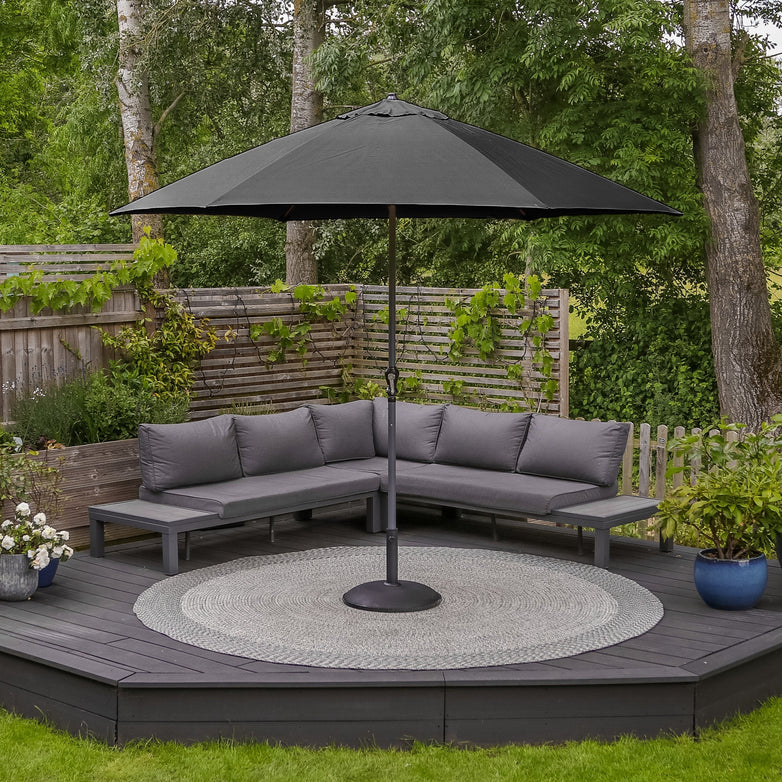 A modern outdoor seating area with gray furniture, a Triton 3m Round Aluminium Parasol in Grey featuring fade-resistant fabric and a UV rating of 50+, and a round rug on a raised wooden deck.