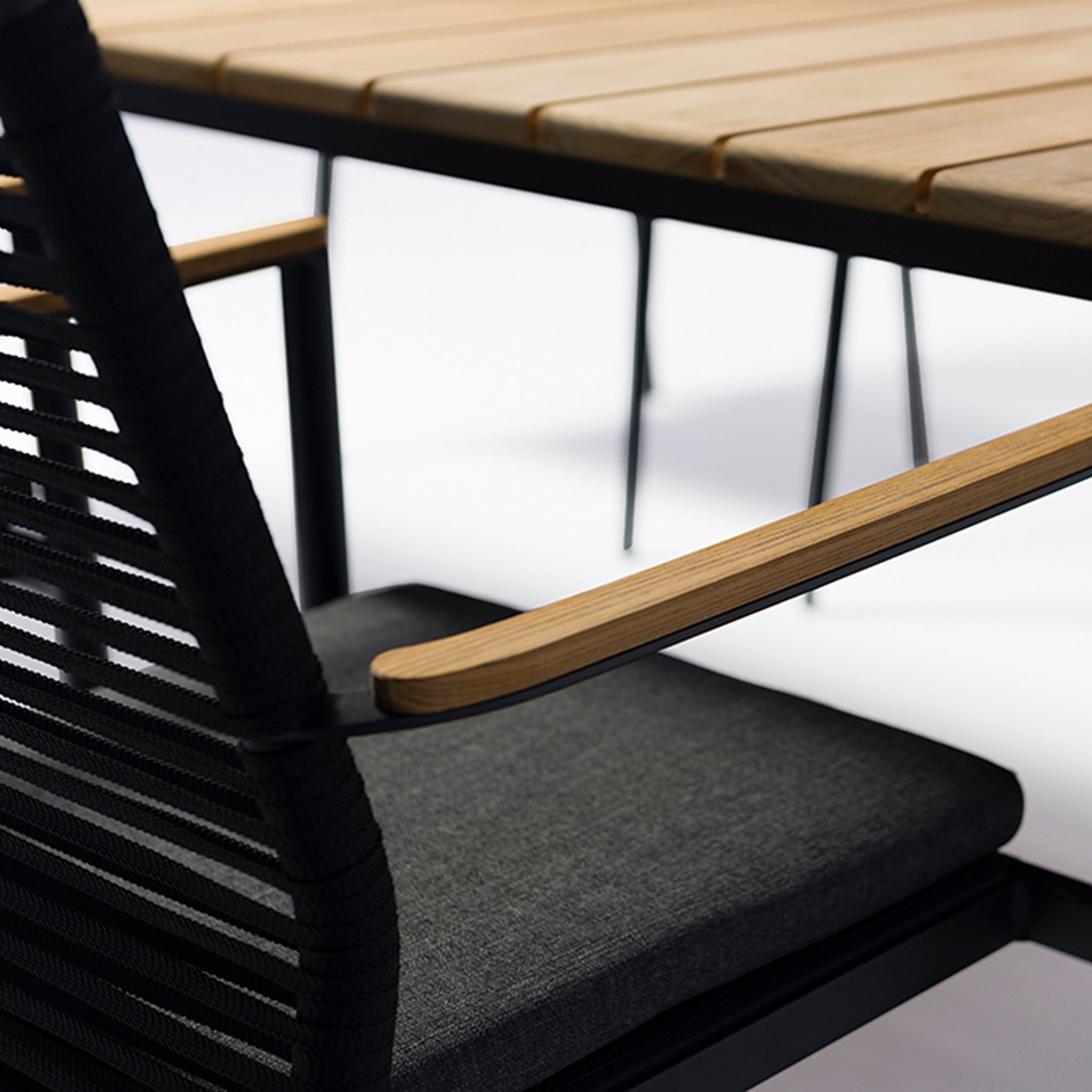 Close-up of a modern outdoor chair featuring a black rope backrest and wooden armrest, next to a matching table. This elegant piece highlights the style and comfort of our Portland 8 Seat Rectangular Dining Set with Teak Table in Charcoal, perfect for garden furniture enthusiasts.