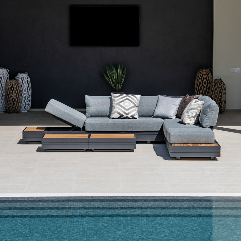 Modern outdoor lounge area featuring a Panama Luxury Outdoor Large Corner Group Set in Washed Grey with grey cushions, decorative pillows, wooden tables made from sustainable teak, and a pool in the foreground.