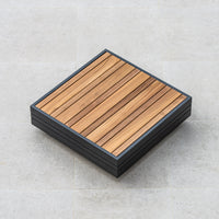 A square Panama Teak Coffee Table with a slatted Teak wooden top and black frame sits on a light-colored tiled floor.