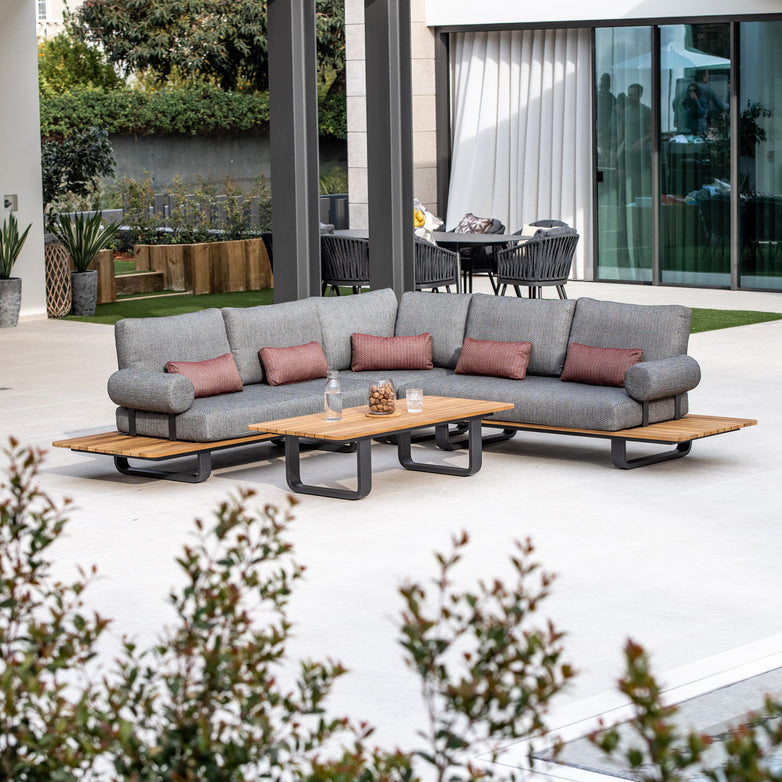 Outdoor patio featuring a spacious Bay Corner Group Set with 4 Waist Pillows in Olive Green, complemented by a teak table and potted plants, all set on an expansive concrete patio.