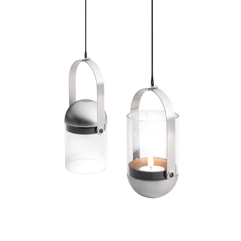 Two modern hanging lanterns, one with a brushed solid stainless steel dome top and the other featuring a Höfats GRAVITY CANDLE Lantern with a lit candle inside, both suspended by thin black cords.