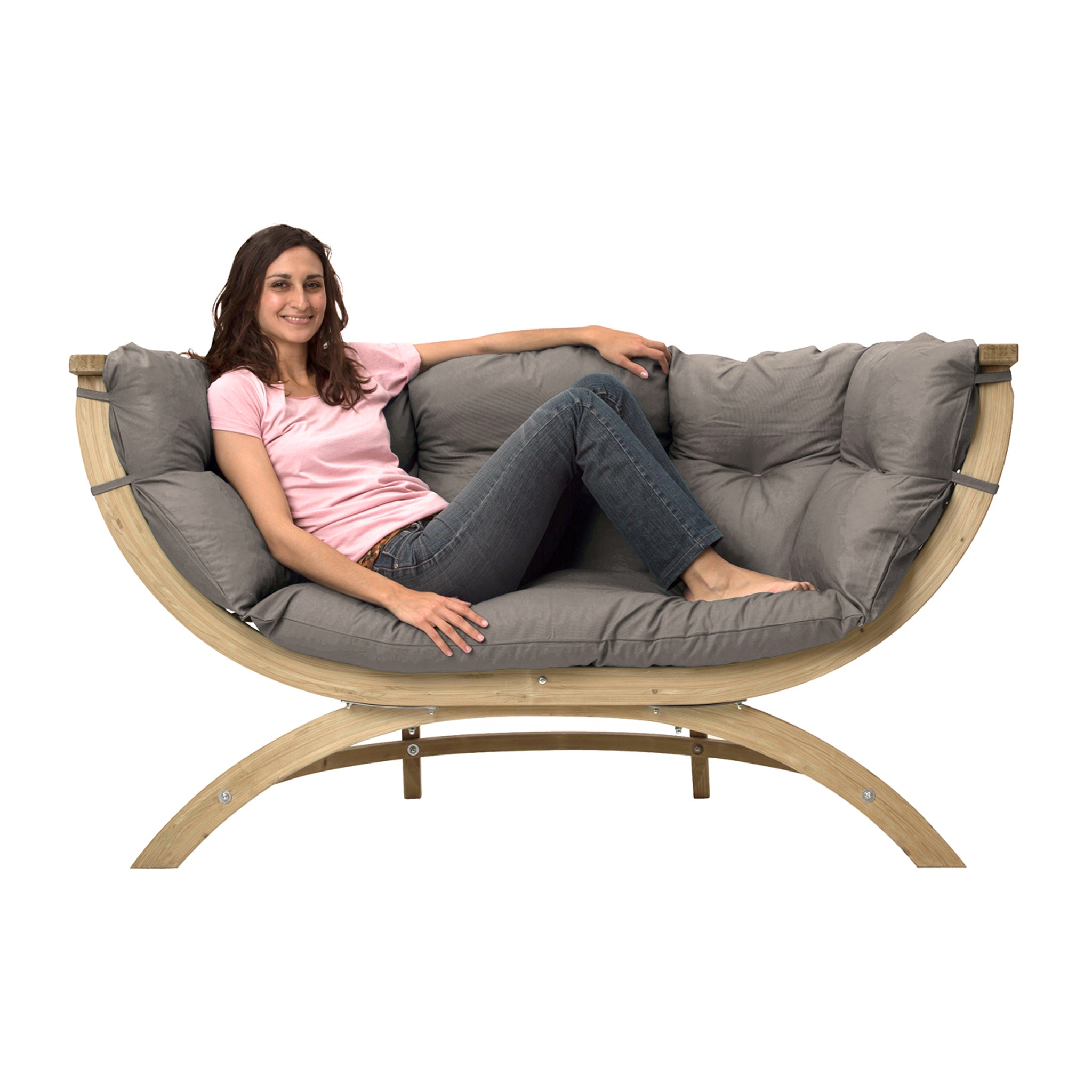 A woman in a pink shirt and jeans lounges on the elegant Globo Siena Due Seat Weatherproof in Taupe Silver, crafted from sustainable wood with a gray cushion, smiling contentedly.