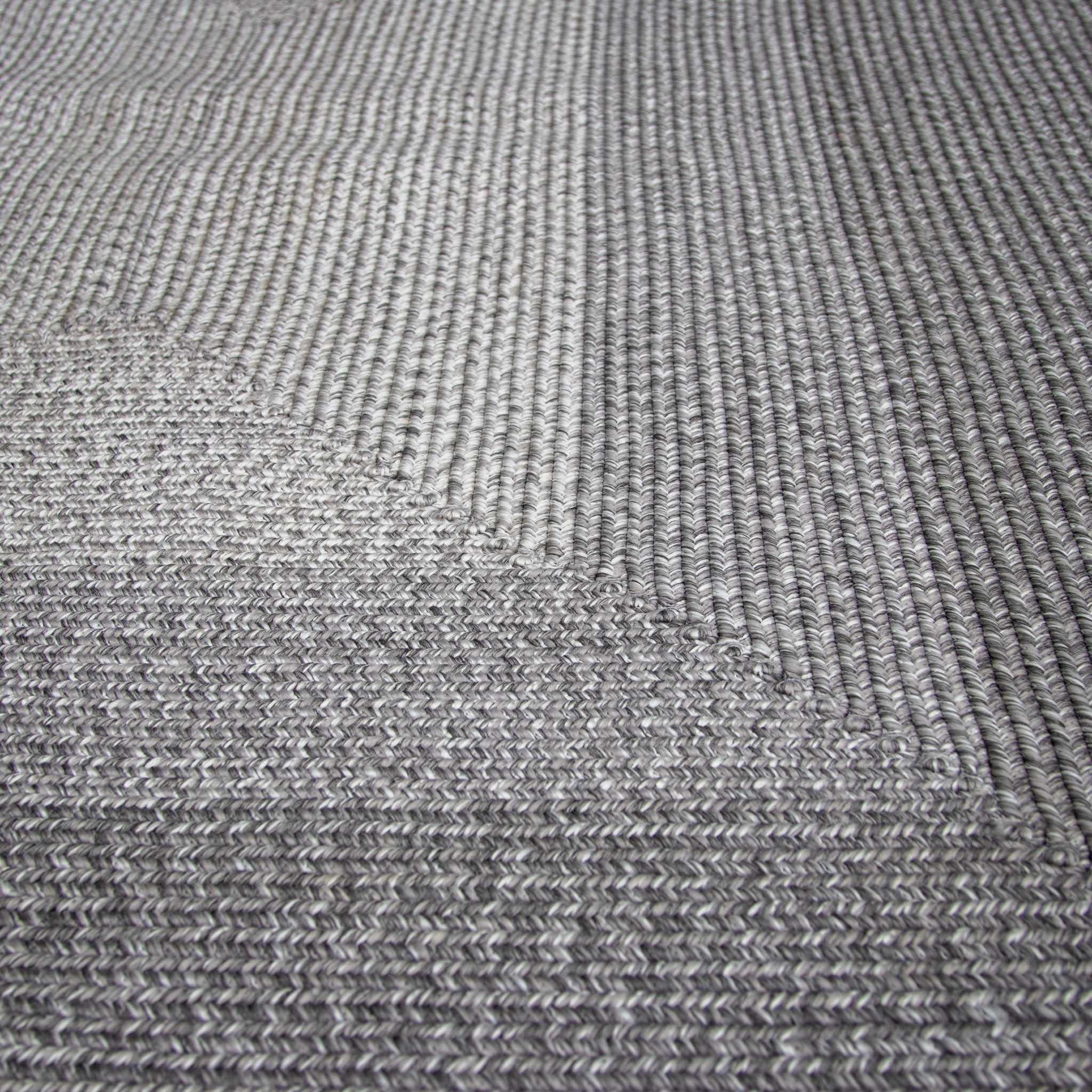 Close-up of the Hestia 366cm x 274cm Weatherproof Indoor and Outdoor Rug in Walnut Grey, a textured gray woven carpet showcasing detailed patterns and variations in the weave, designed to be UV resistant and weatherproof.