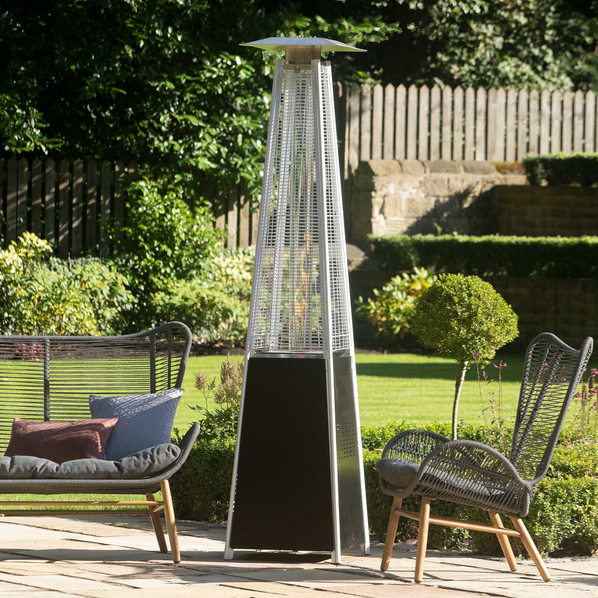 Outdoor patio featuring a Quadrilateral Patio Heater in Black, two wicker chairs, and a lush garden background.