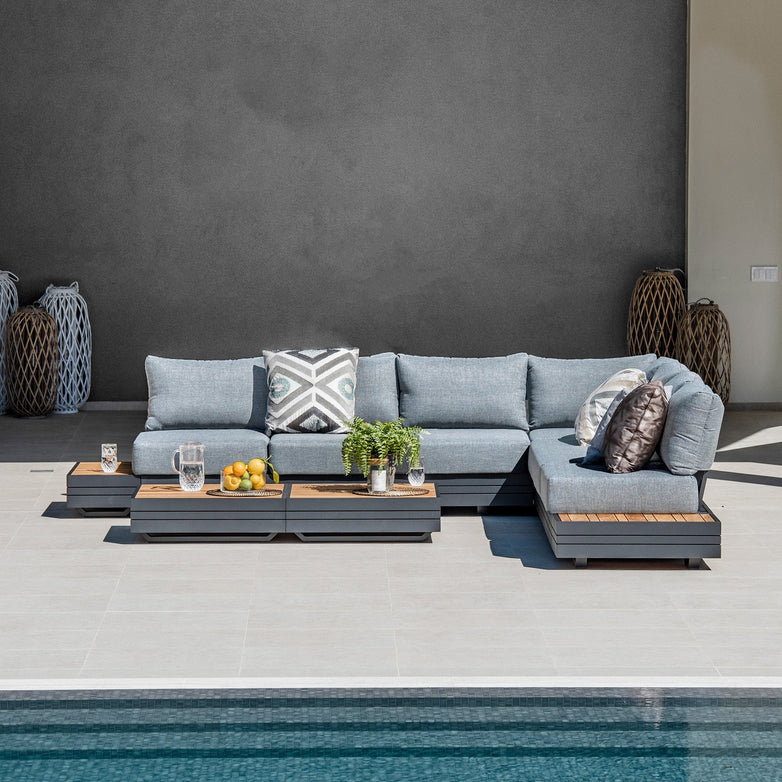 Modern outdoor patio setup with a Panama Luxury Outdoor Large Corner Group Set in Washed Grey, featuring a sustainable teak coffee table, cushions, and greenery-adorned modular sofa set by the pool.