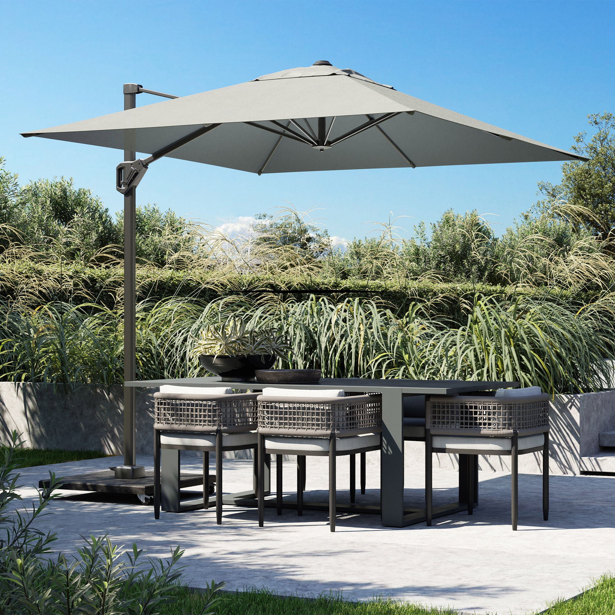 Outdoor dining set with an umbrella, six chairs, and a table in a garden with lush greenery and a clear blue sky. The Voyager T1 3m x 2m Rectangular Parasol in Grey offers 360 degrees rotation for optimal shade throughout the day.